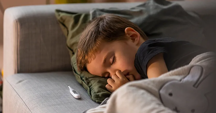 Little boy lying on couch sleeping with thermometer next to him