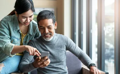 Father and daughter sitting side by side smiling while looking at mobile phone screen