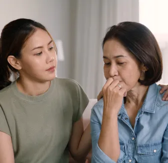 Mother and daughter sitting side by side looking concerned